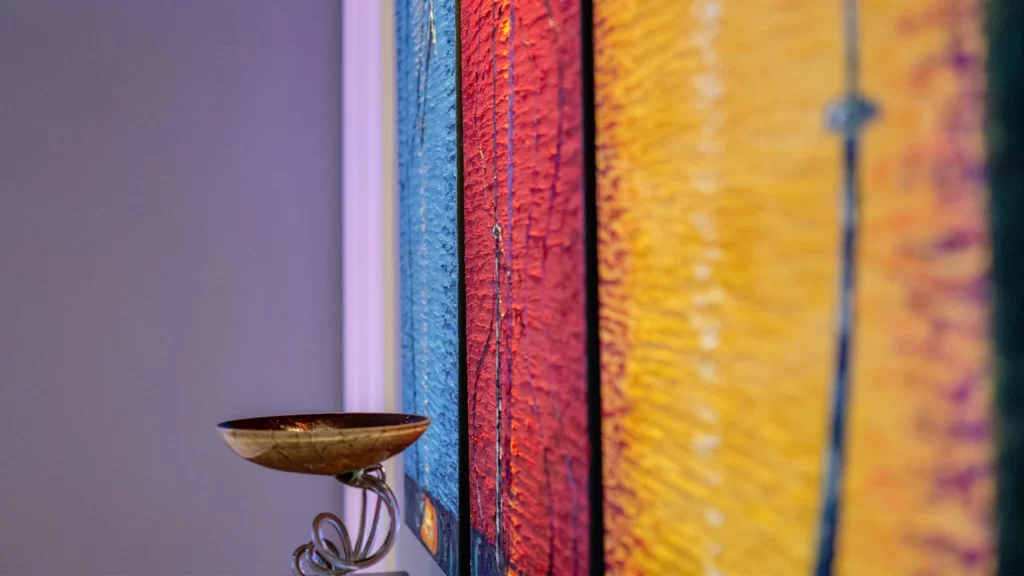 Colorful wall art with textured stripes and an elegant bowl on a decorative stand.