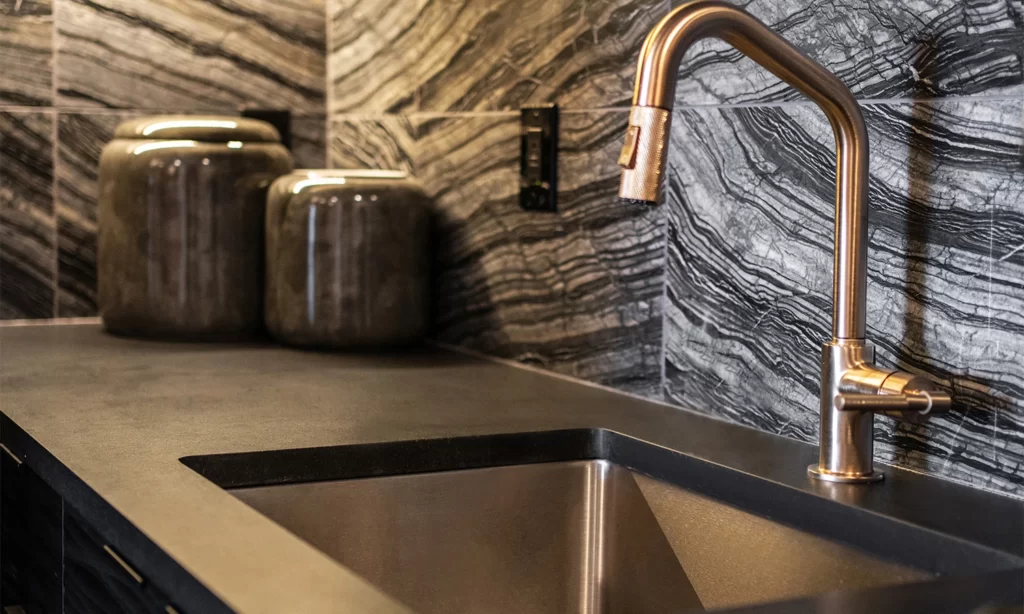 Sleek modern kitchen featuring stainless steel sink, copper faucet, and stylish stone tiles.