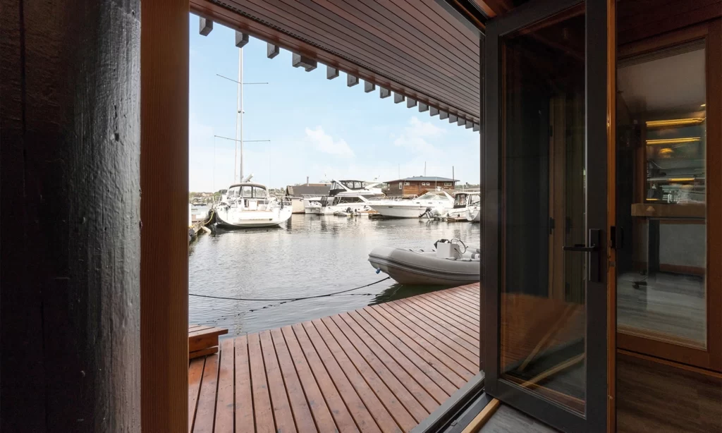 Modern interior opening to a serene marina with boats and a beautiful wooden deck.