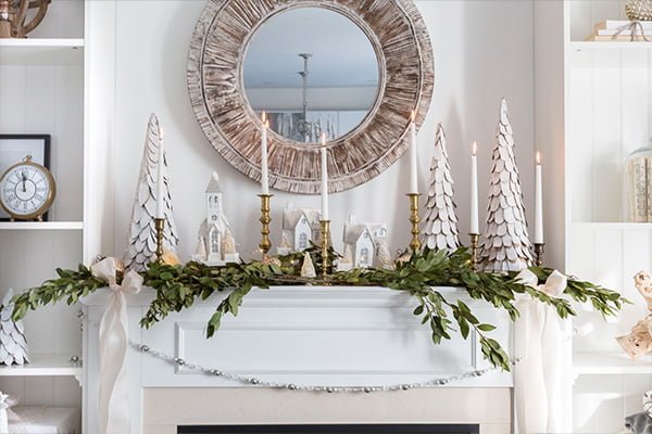 Festive winter mantel decor featuring a mirror, garland, candles, and elegant holiday accents.