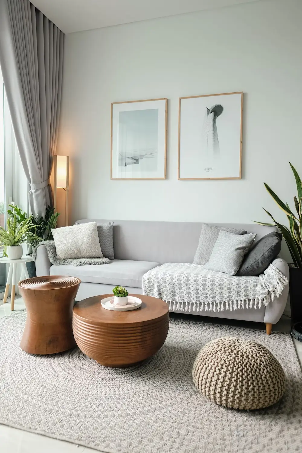 Cozy minimalist living room with light gray sofa, natural light, and vibrant potted plants.