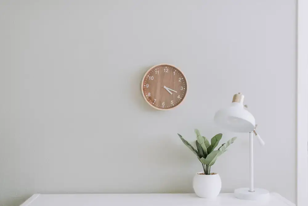 Serene minimalist interior featuring a desk, clock, lamp, and lush potted plant.