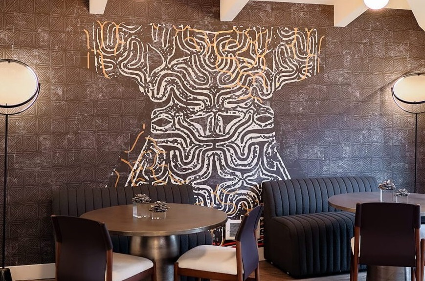 Modern restaurant interior with abstract mural, stylish seating, and warm inviting lighting.