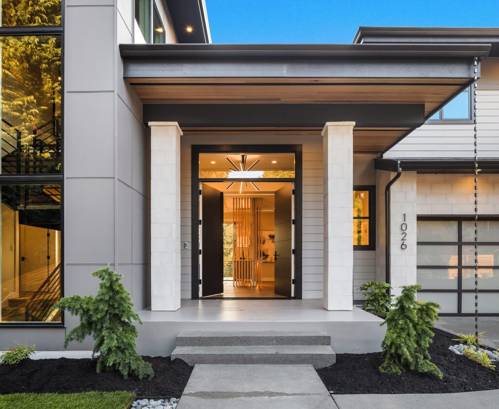 Elegant modern entrance with sleek pillars, inviting glass doors, and lush landscaping.