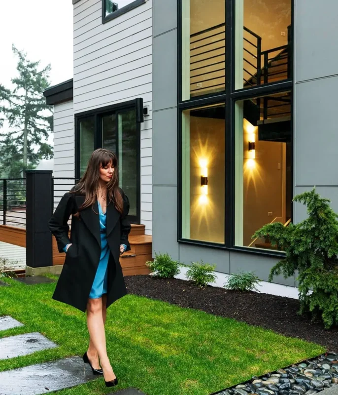 Sophisticated woman in stylish attire walks by a contemporary house with modern architecture.