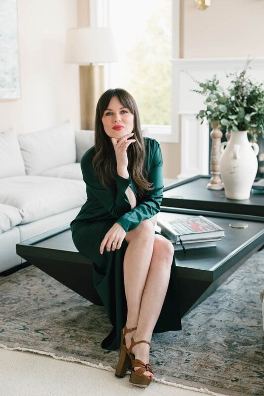 Elegant woman in emerald dress poised on modern coffee table in stylish living room.