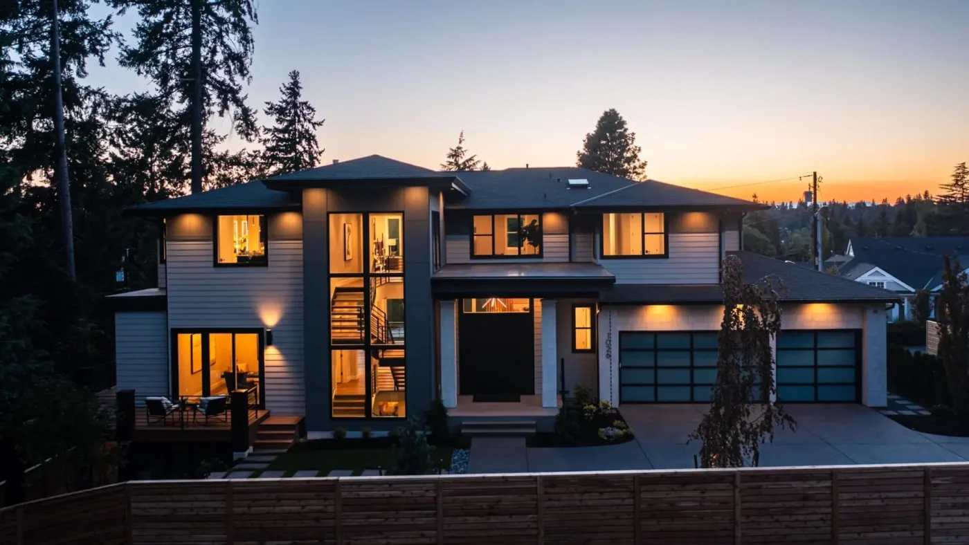 Contemporary two-story home illuminated at twilight, surrounded by lush landscaping and serene nature.