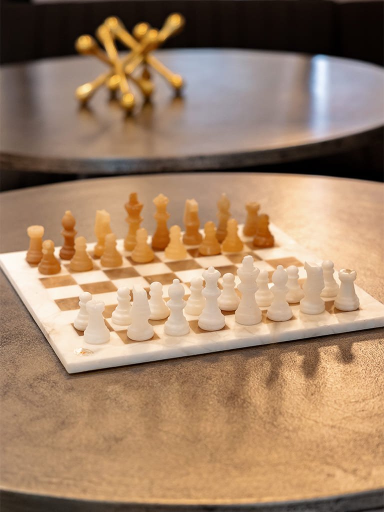 Sophisticated chess set on a round metallic table with artistic decor in the background.