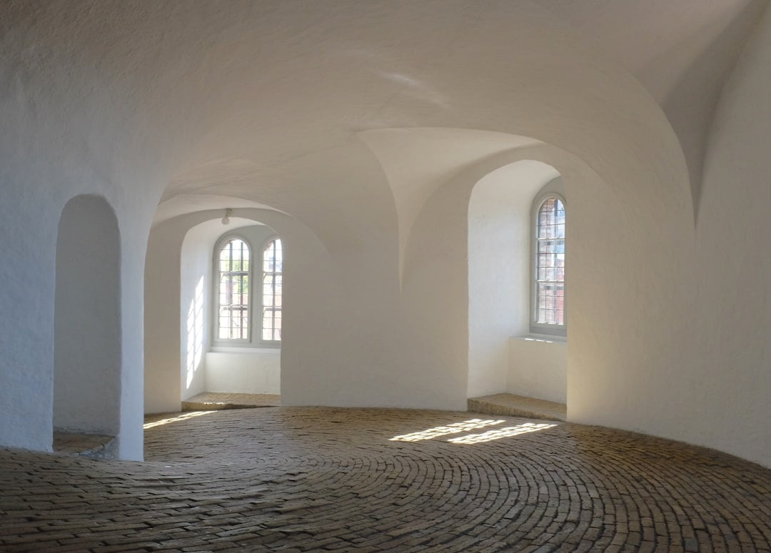 Tranquil minimalist interior featuring elegant arches, bright walls, and textured cobblestone flooring.