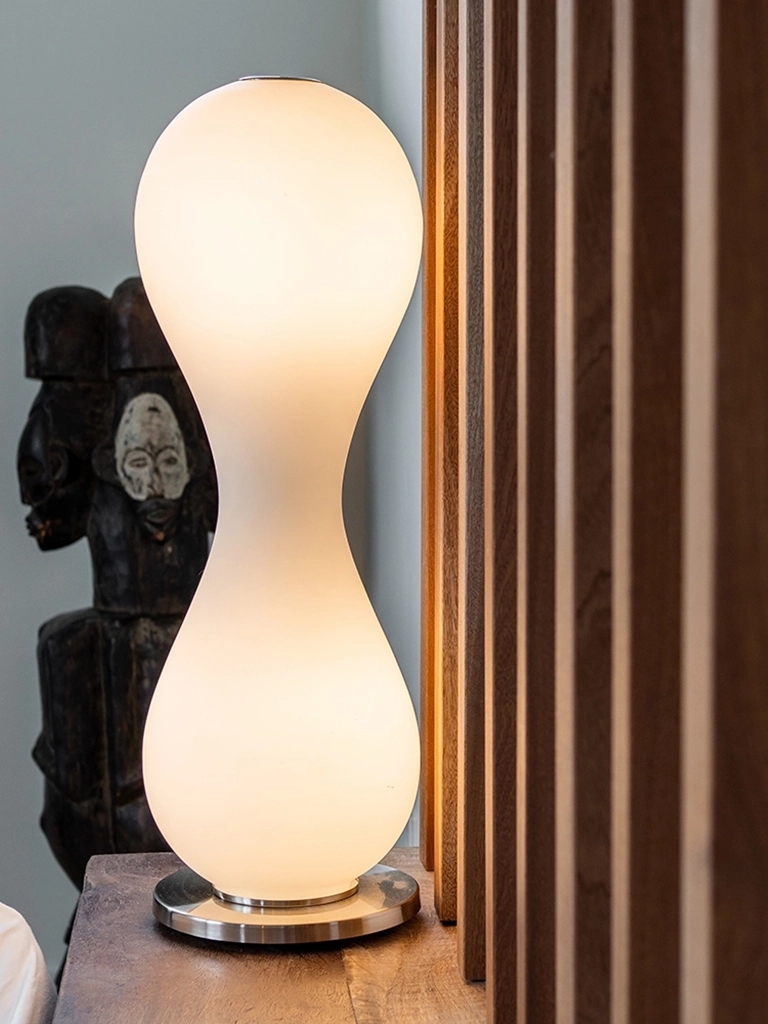 Elegant modern lamp complemented by an intriguing African-inspired sculpture on a polished wooden surface.