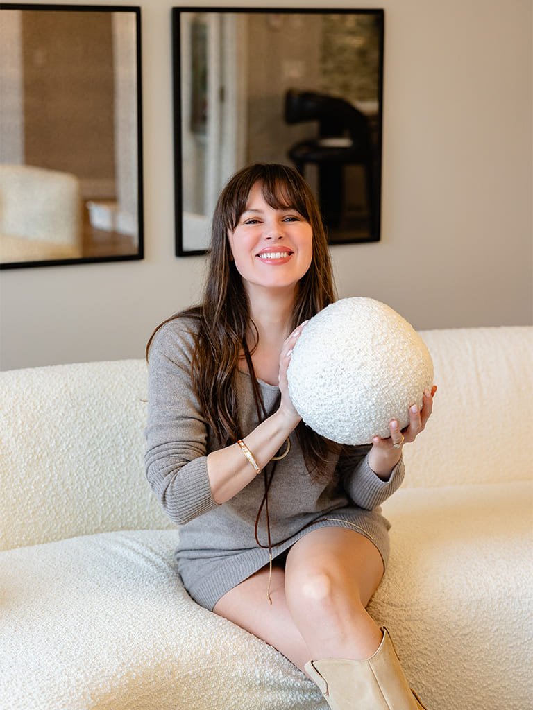 Joyful woman sitting on a cozy sofa, playfully holding a whimsical plush sphere.