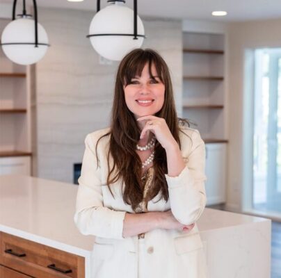 Confident woman in a stylish blazer poses in a modern kitchen, exuding professionalism and warmth.