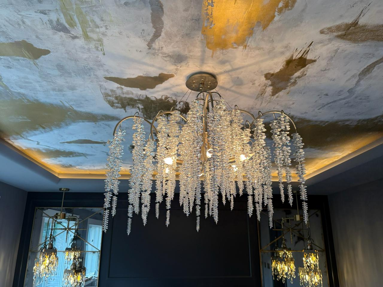 Elegant chandelier hangs from an artistic ceiling, enhancing modern interior luxury and sophistication.