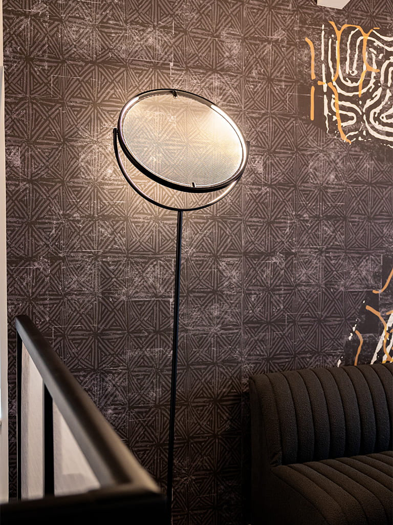 Stylish cozy interior with a sleek floor lamp, dark patterned wallpaper, and plush sofa.