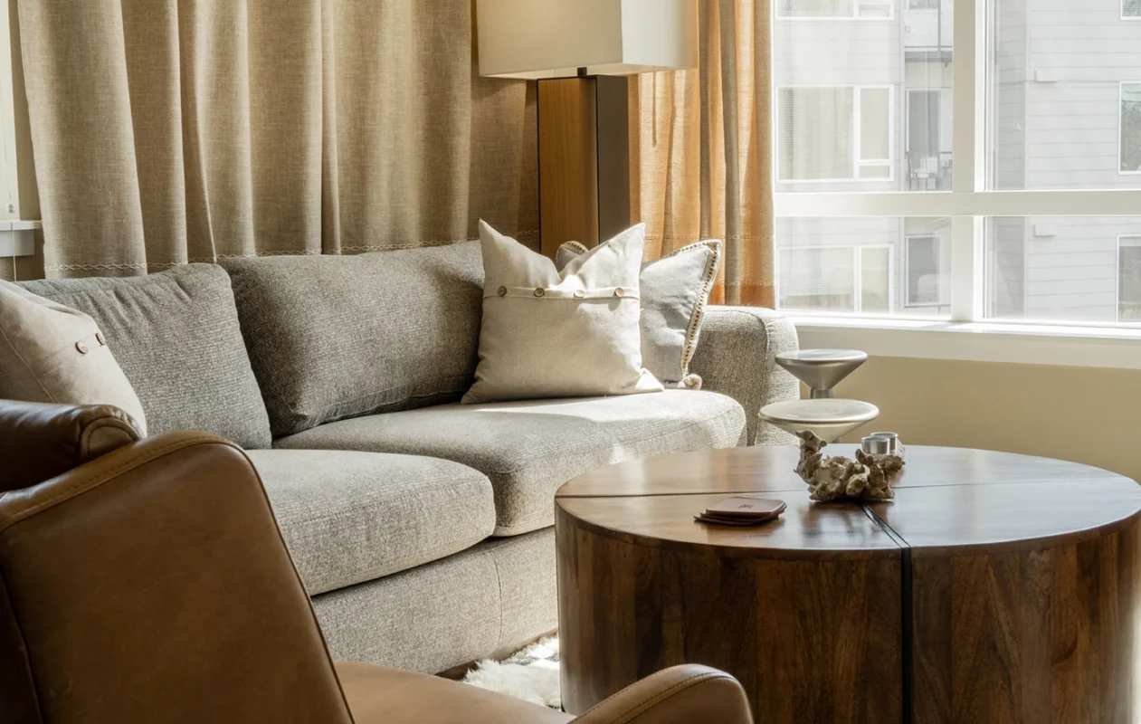 Cozy living room with a gray sofa, wooden coffee table, and natural lighting.