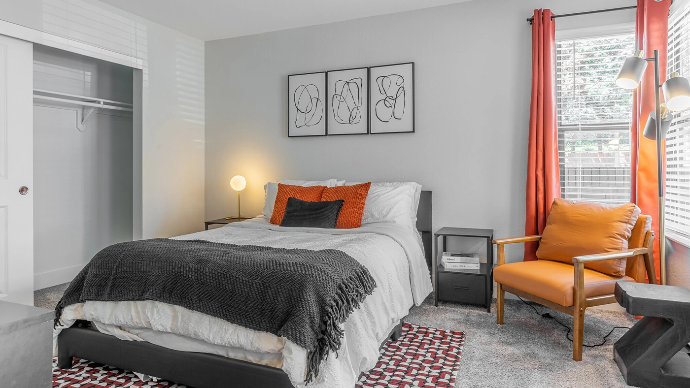 Cozy modern bedroom design with gray walls, white bedding, and vibrant orange accents.