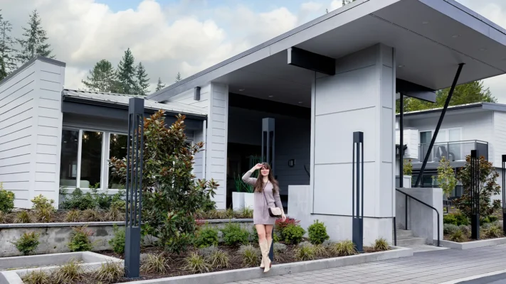 Stylish woman poses outside a modern residential building with landscaped garden and large windows.