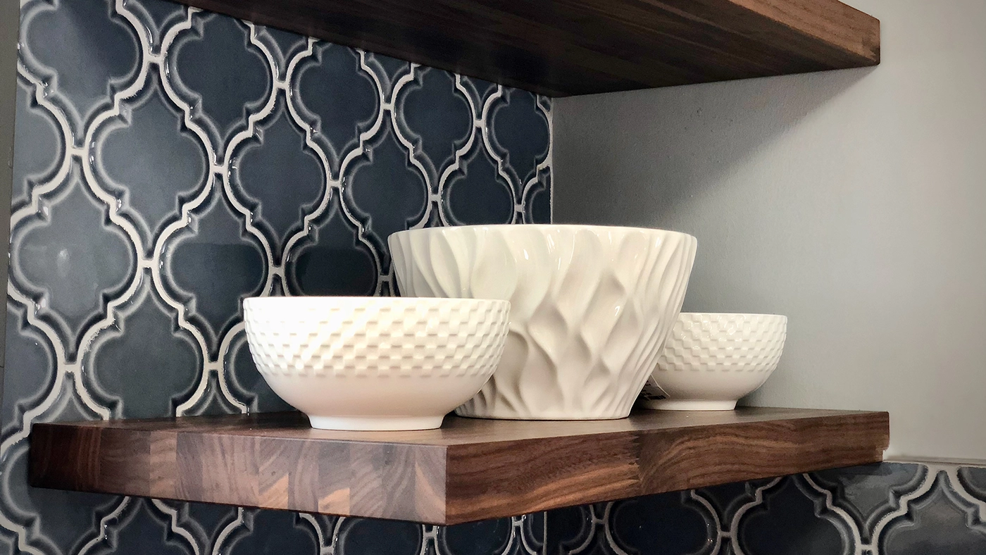 Elegant white ceramic bowls on a dark wood shelf against a decorative blue tiled backsplash.