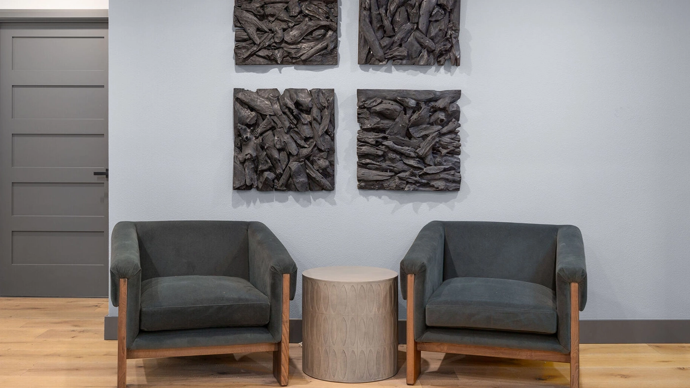 Modern minimalist seating area with cozy gray armchairs and textured artwork for a calming vibe.