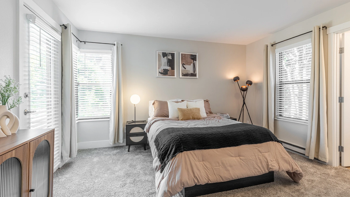 Cozy modern bedroom with earthy tones, plush carpet, and natural light showcasing serene decor.