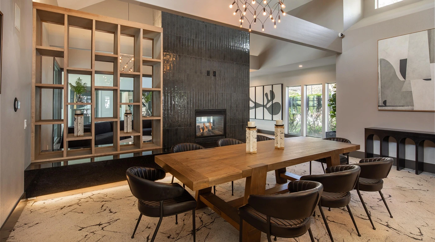 Modern dining area with wooden table, upholstered chairs, decorative shelving, and cozy fireplace.