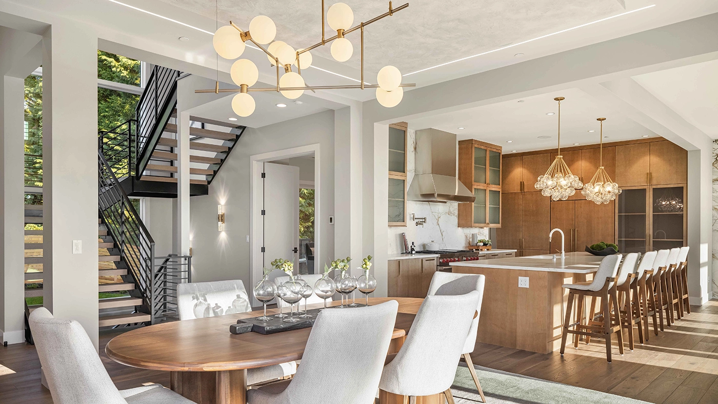 Luxury interior design in Bellevue showcasing seamless open-concept living with walnut wood dining table, brass globe chandelier, white cabinetry, marble island, and integrated kitchen design by ARIID luxury designer