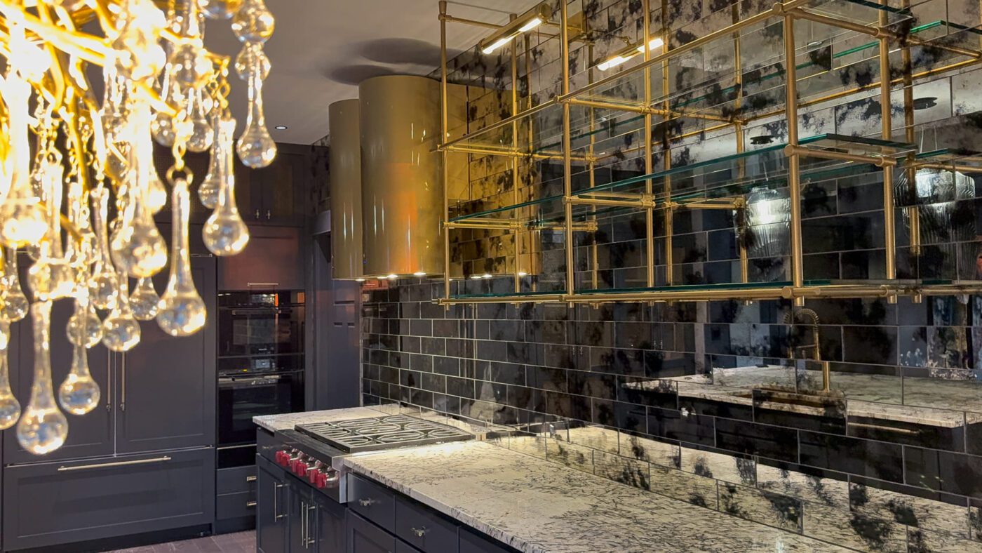 Sophisticated modern luxury kitchen with elegant chandelier, dark cabinetry, and polished stone countertop.