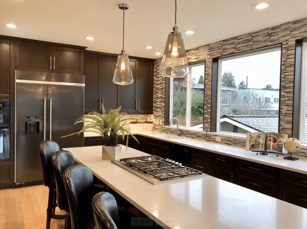 Image of a modern kitchen featuring dark cabinetry, a large island, and large windows showcasing scenic lake views, highlighting luxury interior design in the Pacific Northwest.