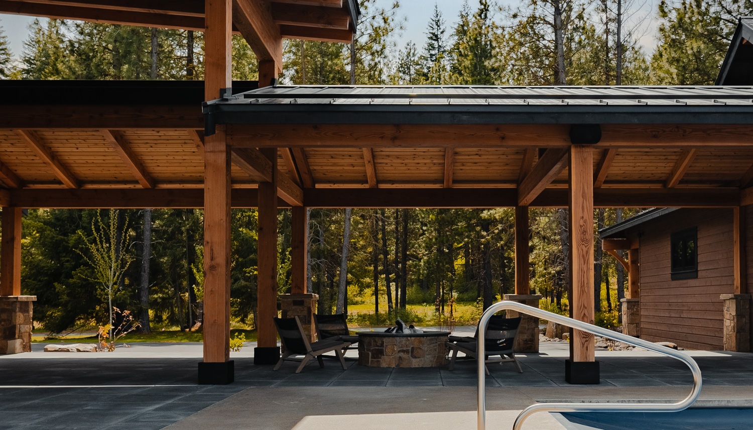 Serene outdoor retreat with wooden overhang, fire pit, and lush greenery perfect for relaxation.