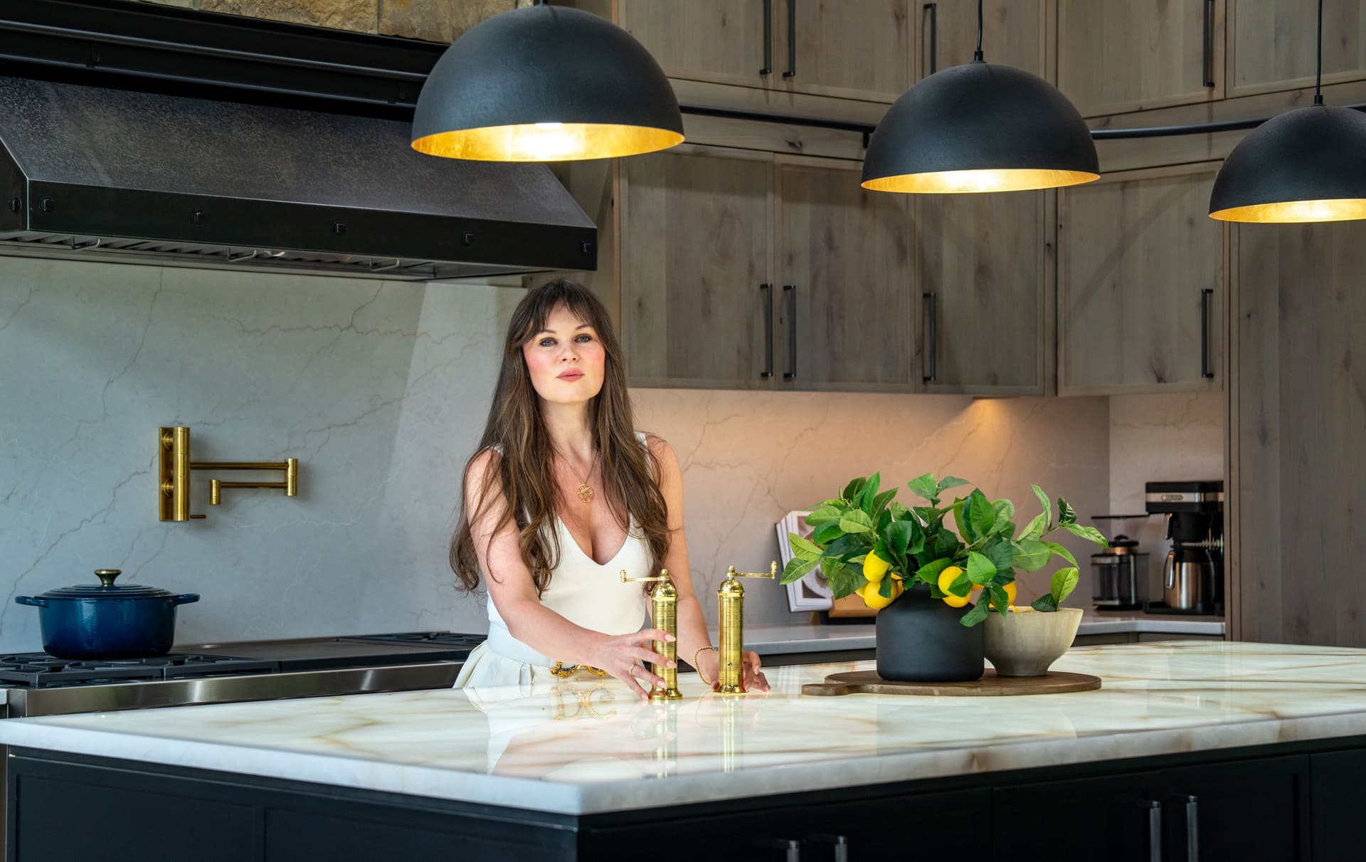 Elegant woman in stylish kitchen with marble island, modern appliances, and fresh greenery.