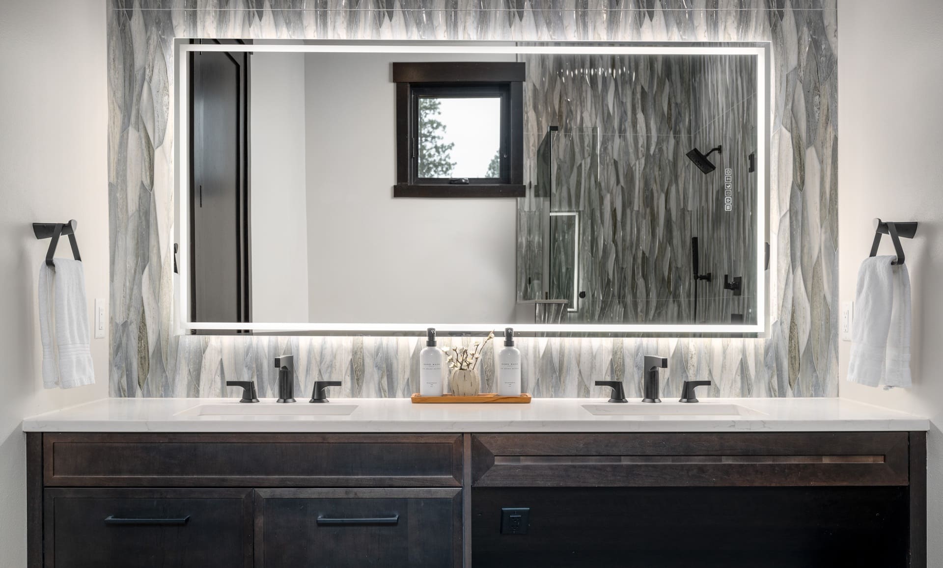 Stylish modern bathroom with double sink vanity, elegant mirror, and textured gray tiles.