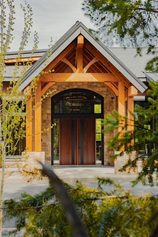 Contemporary house entrance with elegant wooden doors, stone walls, and lush landscaping.