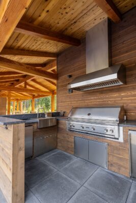 Stylish outdoor kitchen featuring stainless steel grill, granite countertops, and rustic wooden beams.