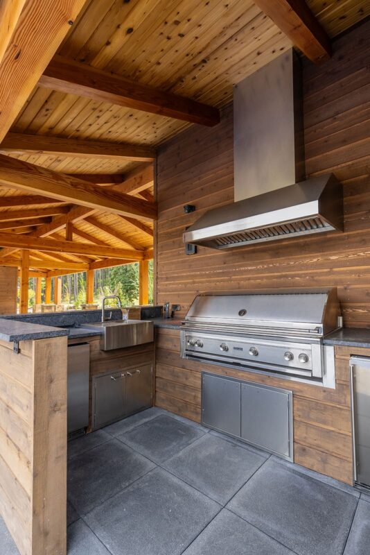 Stylish outdoor kitchen featuring stainless steel grill, granite countertops, and rustic wooden beams.
