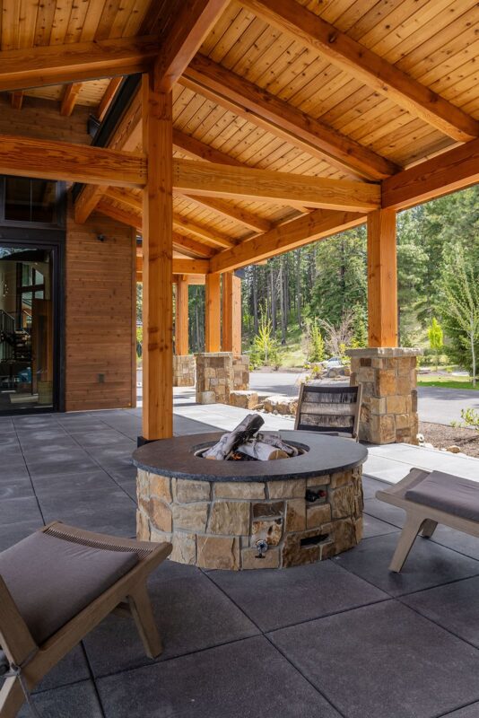 Cozy outdoor living space with a stone fire pit and modern lounge chairs among lush greenery.