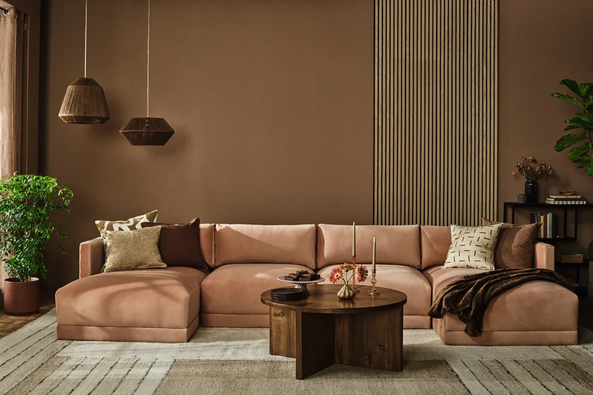 Cozy modern living room featuring a blush pink sectional, dark wood coffee table, and greenery.