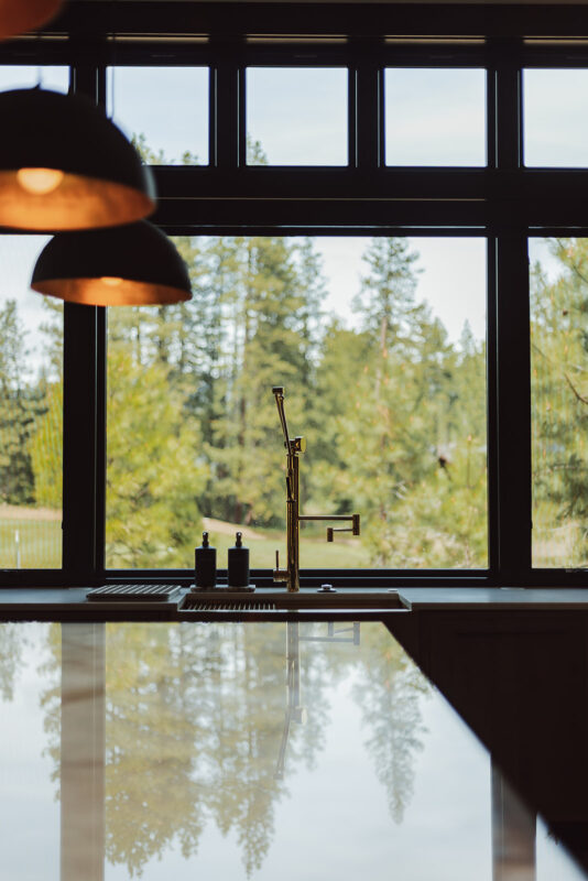 Luxury kitchen sink design featuring brushed gold fixtures, quartz countertops, and expansive forest views in a Suncadia home.