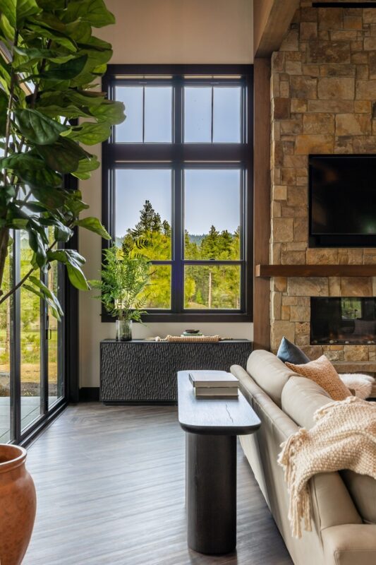 Close-up of console table styled with ceramic vase, gold candleholders, and greenery, placed beneath black-trimmed windows overlooking the forest landscape.