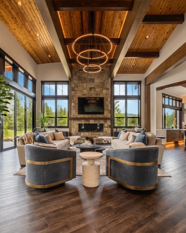 Elegant family room featuring a floor-to-ceiling stone fireplace with mounted TV, dark window frames, and soft neutral seating for a cozy mountain retreat.
