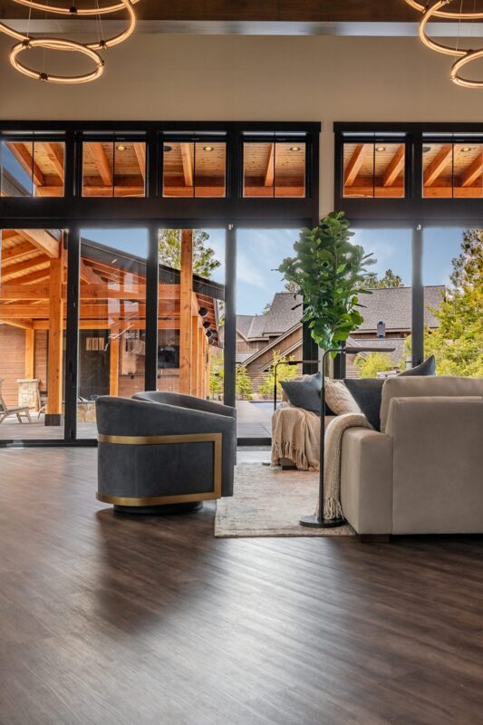 Spacious family room with warm wood beams, modern circular chandeliers, and layered neutral tones that blend contemporary design with rustic mountain charm.
