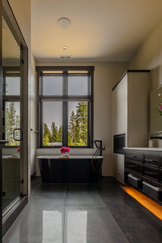 Elegant double vanity with rich wood cabinetry, white countertop, under-cabinet lighting, and fresh floral arrangement enhancing the modern bathroom design.