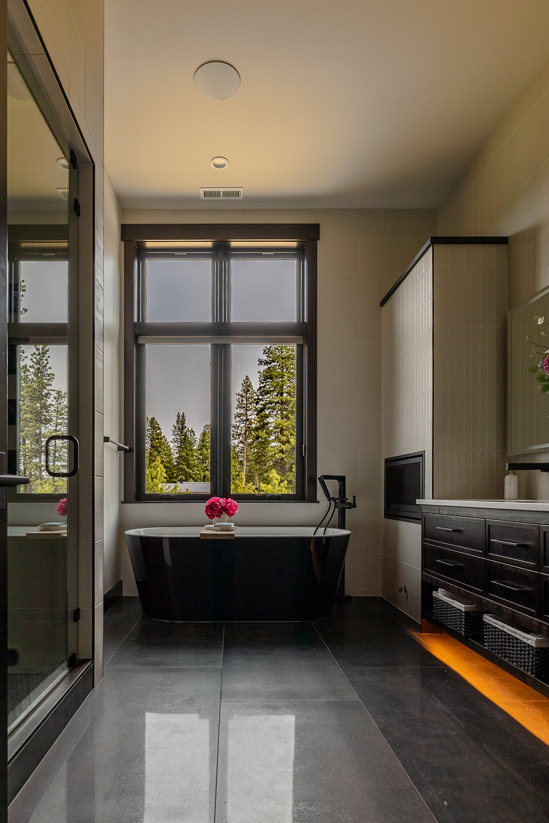 Elegant double vanity with rich wood cabinetry, white countertop, under-cabinet lighting, and fresh floral arrangement enhancing the modern bathroom design.