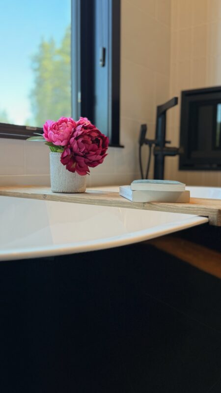 Close-up of a modern bathtub ledge styled with pink peonies and a book, adding warmth, personality, and tranquility to the contemporary space.