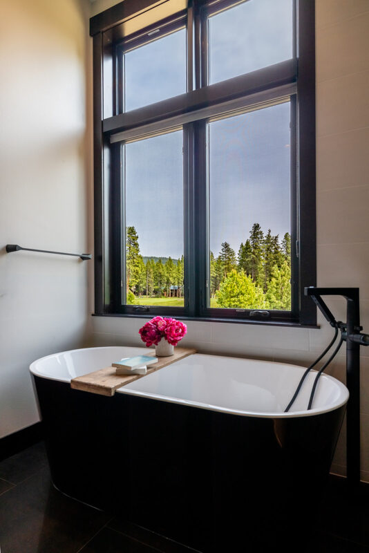 Luxury mountain bathroom by Ariana Designs & Interiors featuring a black freestanding tub, large window view, and warm LED-lit vanity for balance and harmony.