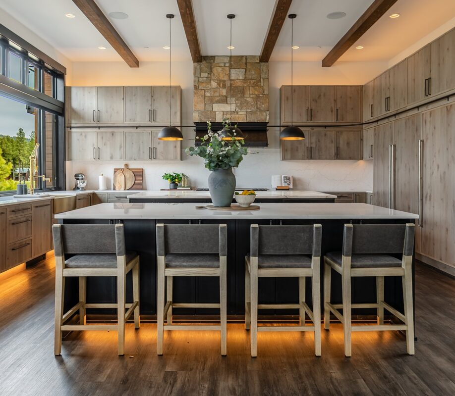 Luxury Suncadia kitchen interior design featuring a black island with seating, wood cabinetry, stone range hood, pendant lighting, and natural mountain views.