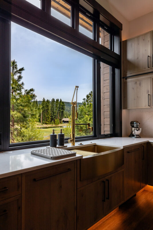 Close-up of gold kitchen faucet and farmhouse sink with panoramic mountain views through large Suncadia window.