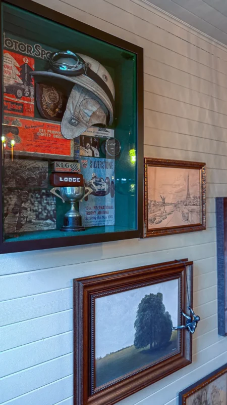 Office hallway wall display featuring a shadowbox with a vintage racing helmet and trophy, a sketch of the Eiffel Tower, and a painting of a large tree.