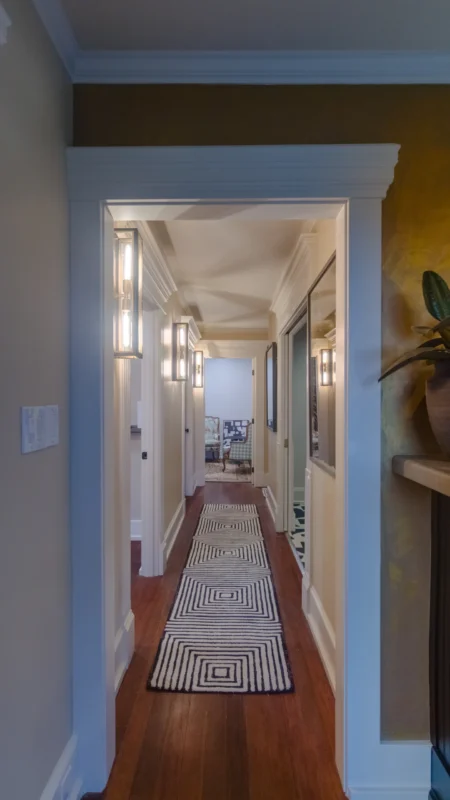 Long, narrow office hallway with dark wood floors, white trim, modern light fixtures, and a black and white geometric patterned runner rug.