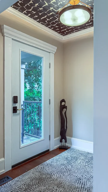 Close-up of the office front door entryway, featuring a tall glass door, a dark wood sculpture, and a ceiling covered in dark, patterned wallpaper.