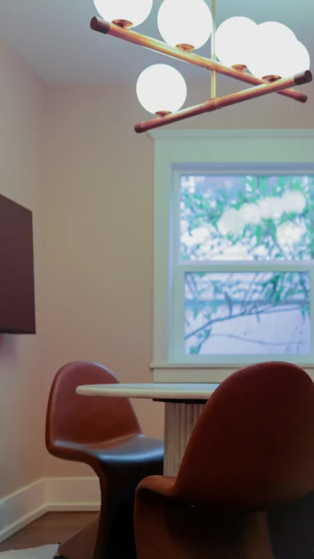 Close-up of two brown leather-look S-shaped meeting chairs and a marble table next to a window, under a modern globular chandelier.